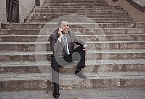 Happy mature business entrepreneur man sitting outdoors urban stairs working and using smart phone