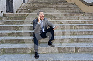 Happy mature business entrepreneur man sitting outdoors urban stairs working and using smart phone