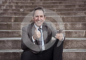 Happy mature business entrepreneur man sitting outdoors urban stairs working and using smart phone