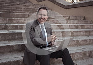 Happy mature business entrepreneur man sitting outdoors urban stairs working and using smart phone