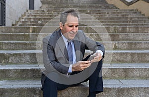 Happy mature business entrepreneur man sitting outdoors urban stairs working and using smart phone