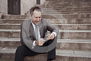 Happy mature business entrepreneur man sitting outdoors urban stairs working and using smart phone