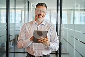 Happy mature business man manager standing in office using digital tablet.