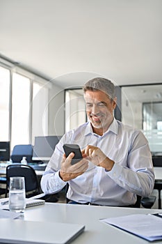 Happy mature business man manager using mobile phone at work in office.