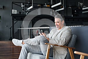 Happy mature business man sitting on chair in office using mobile phone.