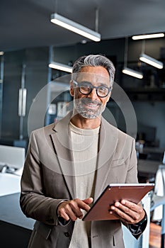 Happy mature business man standing in office using tablet. Vertical portrait