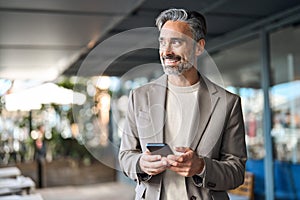 Happy mature business man using phone outdoors. Copy space for ads.