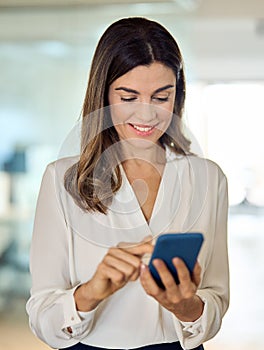 Happy mature business woman holding cellphone, using cell phone in office.