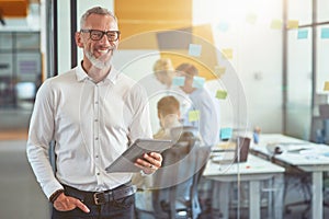 Happy mature businessman in classic wear holding digital tablet, looking at camera and smiling while standing in the