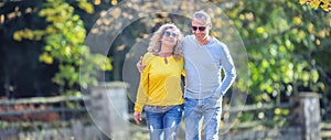 Happy mature couple in autumn park in the embrace walk on the fallen maple leaves