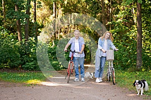 Happy mature couple on bike ride on sunny day on path in forest. Joyful pastime