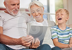A happy mature couple bonding with their grandchild while babysitting and using a digital tablet for video call at home