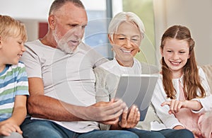 A happy mature couple bonding with their grandchildren while babysitting and using a digital tablet at home