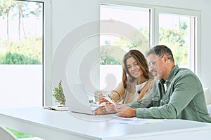 Happy mature couple calculating bills to pay online using laptop at home.