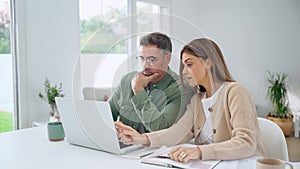 Happy mature couple calculating bills to pay online using laptop at home.