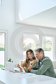 Happy mature couple calculating money expenses using laptop at home. Vertical.