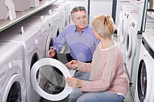 Happy mature couple chooses washing machine for their house in shop of household appliances