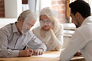 Happy mature couple close deal signing contract with realtor