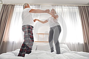 Happy mature couple dancing together on bed at home
