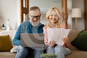 Happy Mature Couple Doing Paperwork And Using Laptop At Home