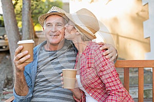 Happy mature couple drinking coffee on a bench in the city