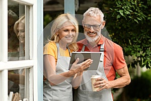 Happy mature couple drinking coffee and using digital tablet outdoors