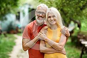 Happy Mature Couple Embracing While Standing Outdoors In Their Garden