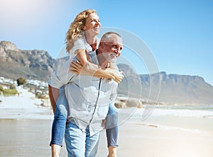 Happy mature couple enjoying vacation by the beach. Active senior husband giving his wife a piggyback ride while