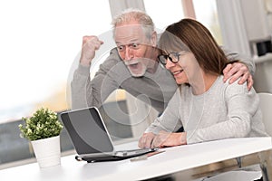 Happy mature couple having a good surprise on laptop