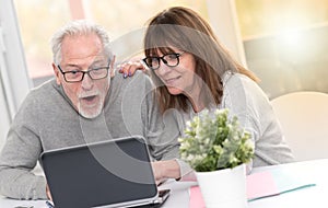 Happy mature couple having a good surprise on laptop, light effect