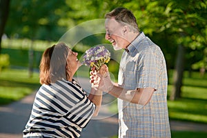 Happy mature couple holding flowers outdoors.