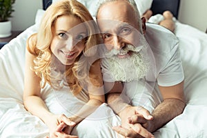 Happy mature couple in love lying together in bed and smiling at camera