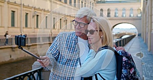 Happy mature couple of tourists making selfie on smartphone in city center.