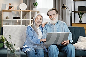 Happy mature couple Using Laptop Watching Movie Together Sitting On Couch At Home.