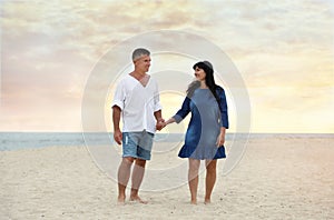 Happy mature couple walking  on sea beach at sunset