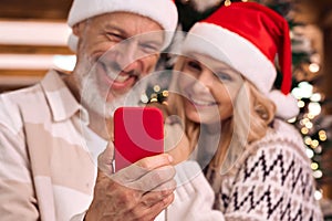 Happy mature family couple in santa hats using cell phone on Christmas.
