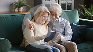 Happy mature family, wife and husband using tablet at home together