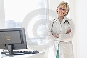 Happy Mature Female Doctor Standing Arms Crossed In Hospital