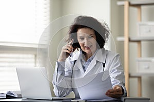 Happy mature female general practitioner consulting patient by phone call.