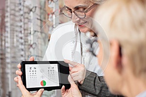Smiling mature female ophthalmologist testing patient`s vision for myopia with a test chart photo