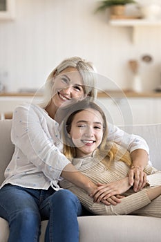 Happy mature grandma and adorable girl resting on home couch