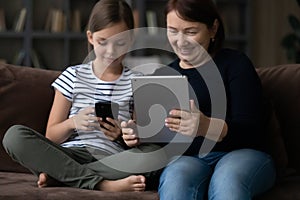 Happy mature grandmother with granddaughter using modern devices together
