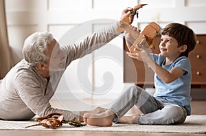 Happy mature grandparent playing with little grandson at home