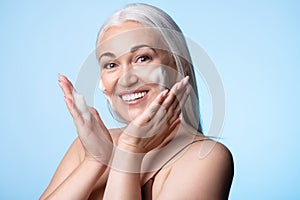 Happy mature gray-haired female washing face by lather having fun