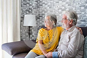 Happy mature husband and wife sit rest on couch at home hugging and cuddling, show care affection, smiling senior loving couple