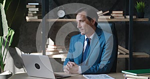 Happy mature male businessman CEO having video call using laptop computer while sitting at office desk. Man in business