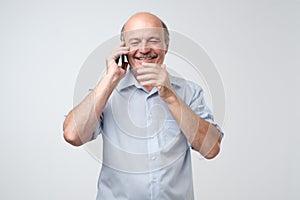 Happy mature man bald and with mustache talking on mobile, on white background