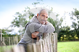 Happy mature man in countryside leaning on wood fence