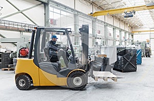 Happy mature man fork lift truck driver lifting pallet in storage warehouse and looking at camera.