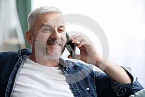 Happy mature man having conversation on smartphone at home